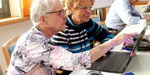 Zwei ältere Frauen sitzen vor einem Laptop. Die ein erklärt der ändere, wie etwas geht