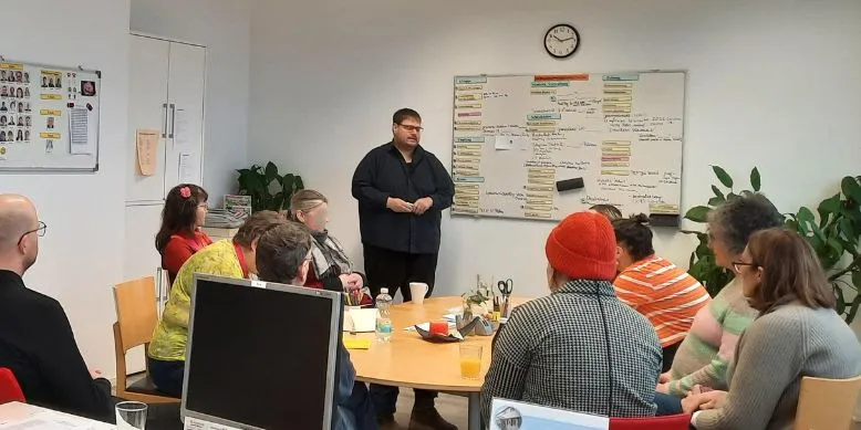 besprechung im clubhaus schwalbennest, mehrere menschen sitzen am tisch, ein mann stecht am whitebooard